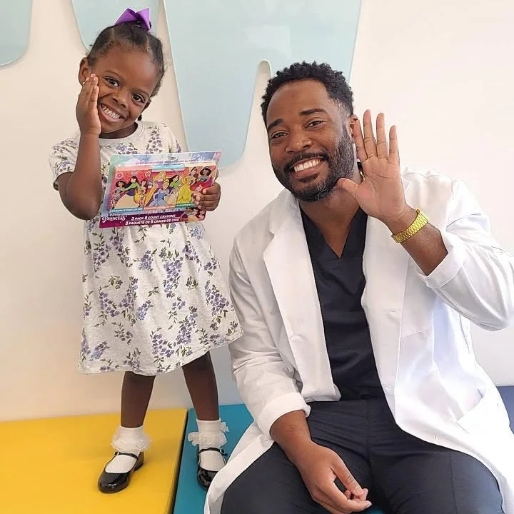 Dr. Ray Tucker waving next to a smiling young patient holding a princess crayon set